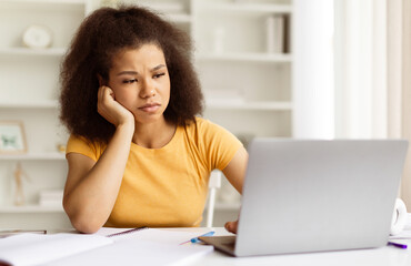 Tired or frustrated African American female student looking unhappy at her laptop, upset black lady...