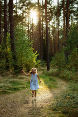 Happy little girl running on a forest path with golden sunlight streaming through tall trees for...