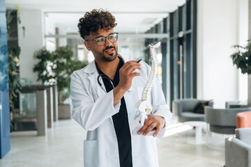Model of human spine in hand. Doctor is indoors in the modern building