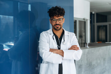 With arms crossed. Doctor is indoors in the modern building