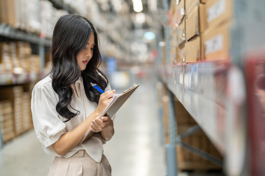 Asian warehouse staff woman checking inventory with clipboard in logistics management, working in supply chain, e-commerce, shipping, warehouse management and distribution center industry business