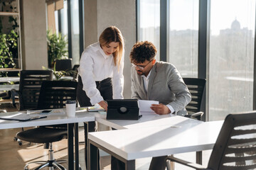 Digital tablet and documents. Man and woman are indoors in modern building