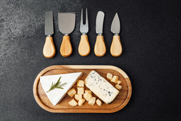 Various cheese types arranged on a wooden platter with cutting utensils