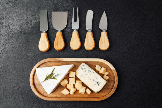 Various cheese types arranged on a wooden platter with cutting utensils
