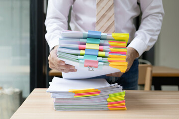 A man is working in an office. On his desk are several sheets of paper, a notebook, a laptop, a...