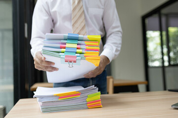 A man is working in an office. On his desk are several sheets of paper, a notebook, a laptop, a...