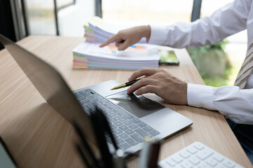 A man is working in an office. On his desk are several sheets of paper, a notebook, a laptop, a calculator, and a pen. The man is staring intently.

