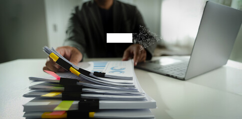 Digital Transformation person working desk with laptop and large stack of documents, holding pen, modern office environment, with focus paperwork
