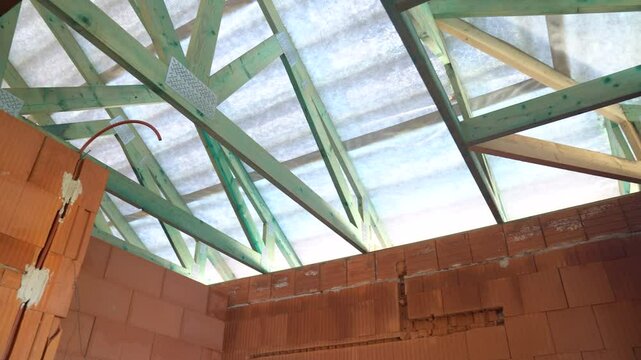 Exposed timber roof trusses above unfinished brick walls inside house under construction
