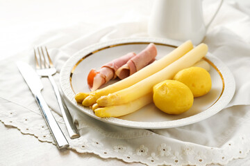 White asparagus, potatoes and boiled ham on a white plate with napkin and cutlery, traditional, seasonal meal, copy space, selected focus