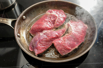 Fresh raw beef steaks are seared in hot oil with plenty of steam in a carbon steel frying pan, cooking meat, selected focus