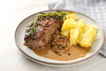 Roasted beef steak with boiled potatoes, sauce and herb garnish on a plate and a white wooden table, homemade meat meal, copy space, selected focus