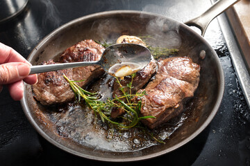 Freshly roasted beef steaks are napped with butter garlic, thyme and rosemary in a carbon steel frying pan, homemade cooking a tasty meat meal, selected focus