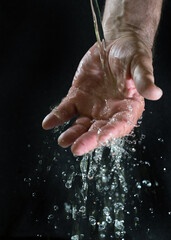 Water running over a hand of a man and splashing glittering drops against a black background, concept for the sustainable living environment on earth, health and hygiene, copy space