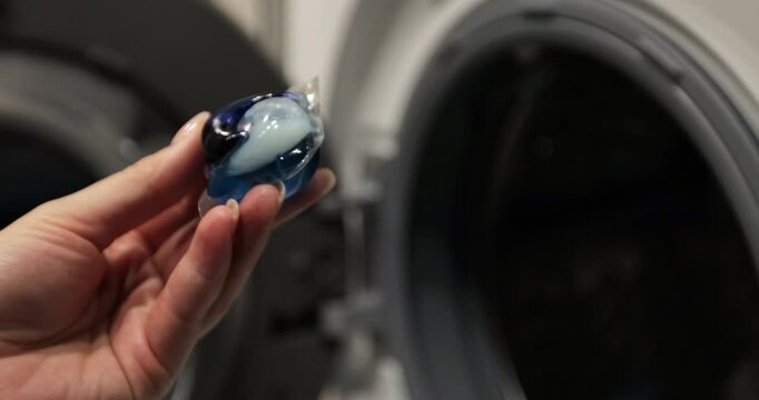 Close up woman puts colorful gel capsules with laundry detergent in the washing machine on dirty laundry. Modern liquid detergents.