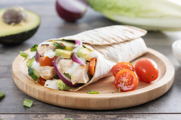 A delicious grilled chicken wrap with vegetables and avocado on wooden table	