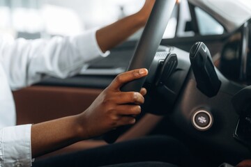 Two hands are on the steering wheel. Woman in white shirt is in the modern car