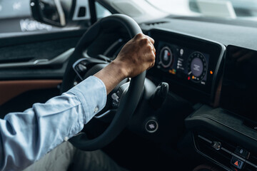 Hands are on the steering wheel. Man in shirt is in the modern car
