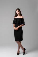 Elegant woman in a black off-the-shoulder dress posing confidently against a neutral background