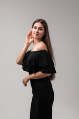 Young woman poses elegantly in a black off-shoulder dress with cascading ruffles in a minimalistic...