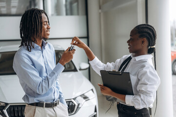 Taking keys, happy owner. Car seller is assisting client in the automobile salon
