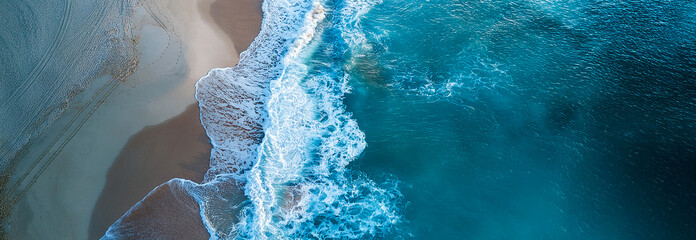 Aerial view down of bluish ocean smaller waves crashing onto the shore of a white sandy beach