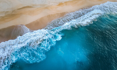 Fototapeta premium Aerial view down of bluish ocean smaller waves crashing onto the shore of a white sandy beach