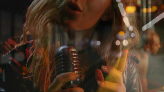 Female singer gripping mic singing in music rehearsal shifting lights behind guitarist strumming