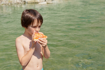 Boy standing in river water and eating pizza