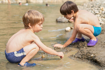 Two boys playing with river mud on the bank of a mountain river