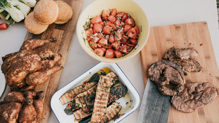 A table with a variety of meats and vegetables, including chicken, beef, and tomatoes. The table is set for a meal, with a knife and a spoon nearby. Scene is inviting and appetizing