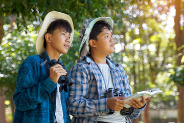 Two Asian boys use binoculars to study the local birds in a community forest. Soft and selective focus.