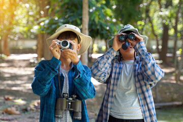 Two Asian boys use binoculars and a camera to study the local birds in a community forest. Soft and selective focus.