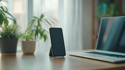Modern workspace with sleek closed laptop and smartphone on a wooden desk near potted plants and bright natural light in a contemporary home office setting