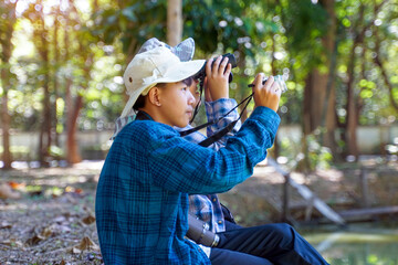 Two Asian boys use binoculars to study the local birds in a community forest. Soft and selective focus.