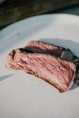 A piece of meat is cut in half and is sitting on a white plate. The meat is pink and has a slightly charred appearance. Concept of indulgence and satisfaction, as the meat is cooked to perfection