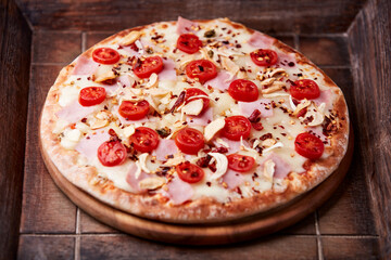 Pizza with ham, cherry tomatoes and mozzarella cheese. Wooden background. Soft focus. Close up.	