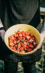 A person is holding a yellow bowl filled with tomatoes and onions. The bowl is placed on a table