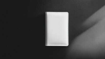 Minimalist white leather-bound planner or notebook with stitched edges on dark background with shadow and subtle lighting for professional office or creative workspace decor