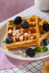 Belgian waffles with blueberries, honey and mint on a white plate. Breakfast with a cup of coffee and sweet waffles.
