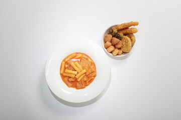 Korean Rose Tteokbokki, a creamy spicy rice cake dish topped with cheese, served with assorted fried snacks. A popular K-Food fusion dish enjoyed for its rich flavor and texture.