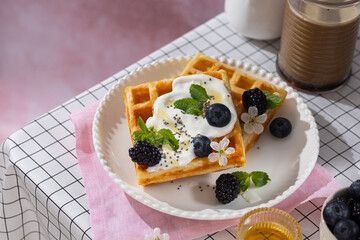 Belgian waffles with blueberries, honey and mint on a white plate. Breakfast with a cup of coffee and sweet waffles.
