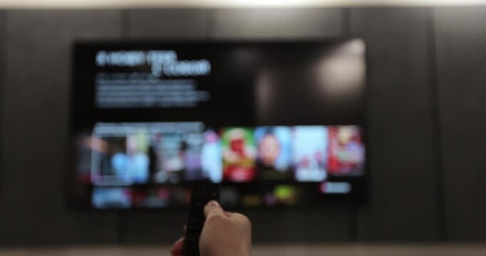 Woman hand selects tv channels with remote control at living room on sofa. Man controls TV using a modern remote control. Close up view.