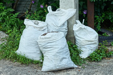 four large protective polyester white packed heavy discarded dirty garbage bags stand near gray concrete pillar on ground during daytime on street
