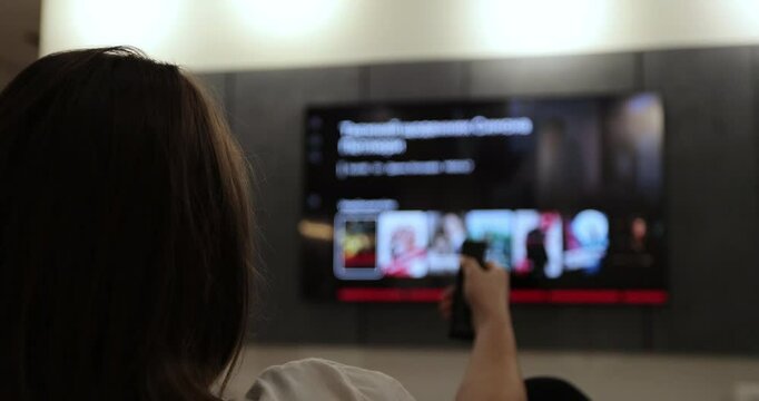 Woman operating a remote control for a smart TV. Channel surfing, focused on the hand and remote control.