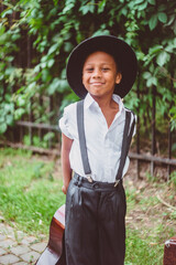 a happy boy dressed in the style of the 20s holds a guitar by the neck behind his back