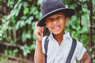 boy dressed in the style of the 20s smiles with all his teeth with one hand holding the brim of his hat
