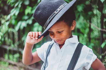 boy dressed in the style of the 20s lifts his hat, holding it by the brim, looking down