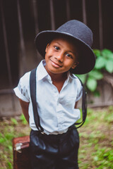 a boy dressed in the style of the 20s with a suitcase on his back looks ingratiatingly at the camera