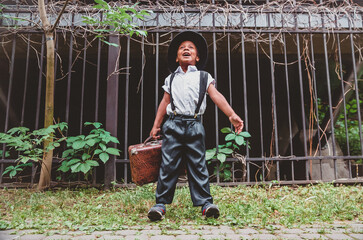 a boy dressed in the style of the 20s with a suitcase in his hand against the background of a fence takes a big breath of fresh air